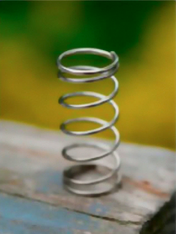 Photo of a metal coil spring standing on a wooden plank
